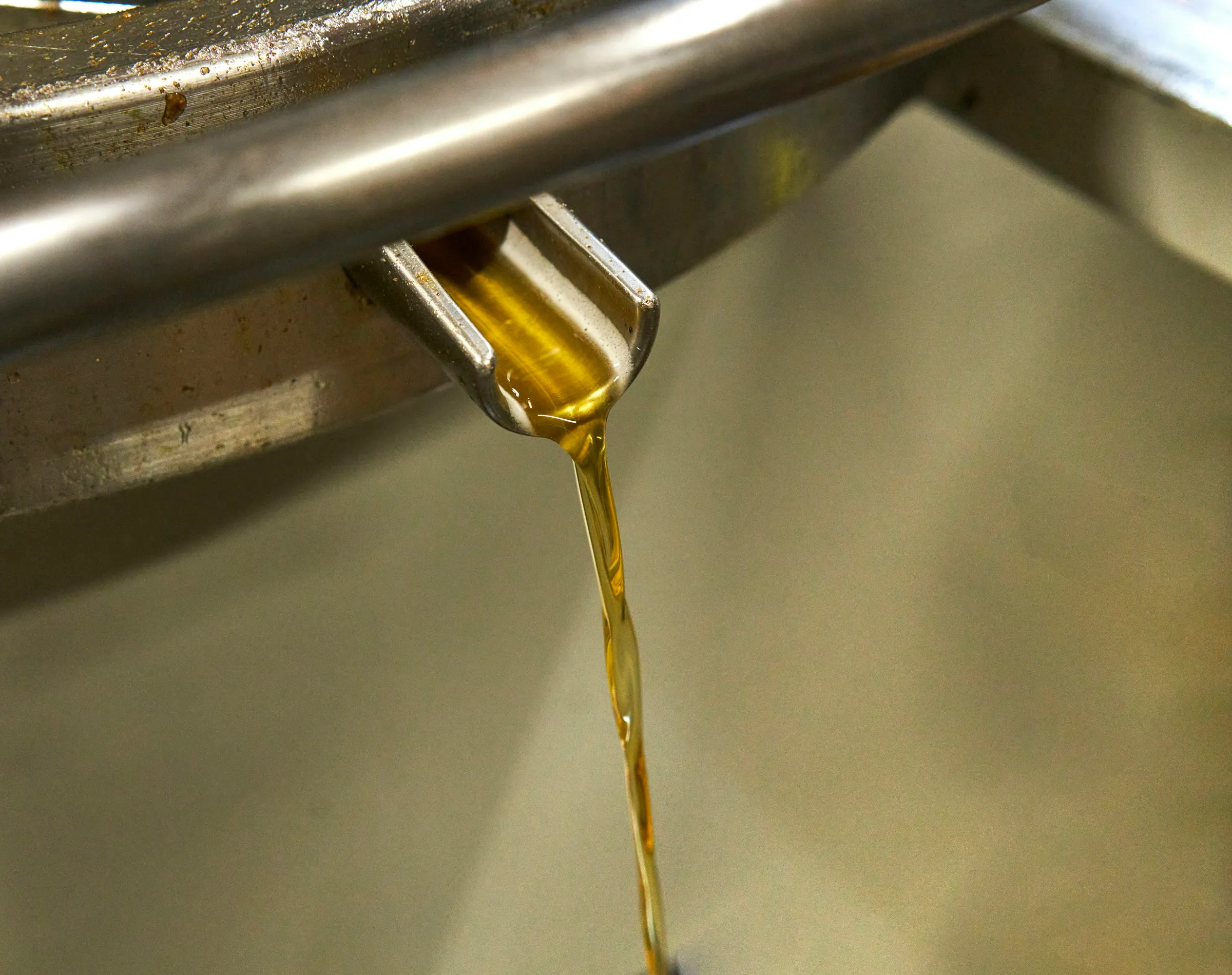Aceite dorado cayendo desde una boquilla metálica.