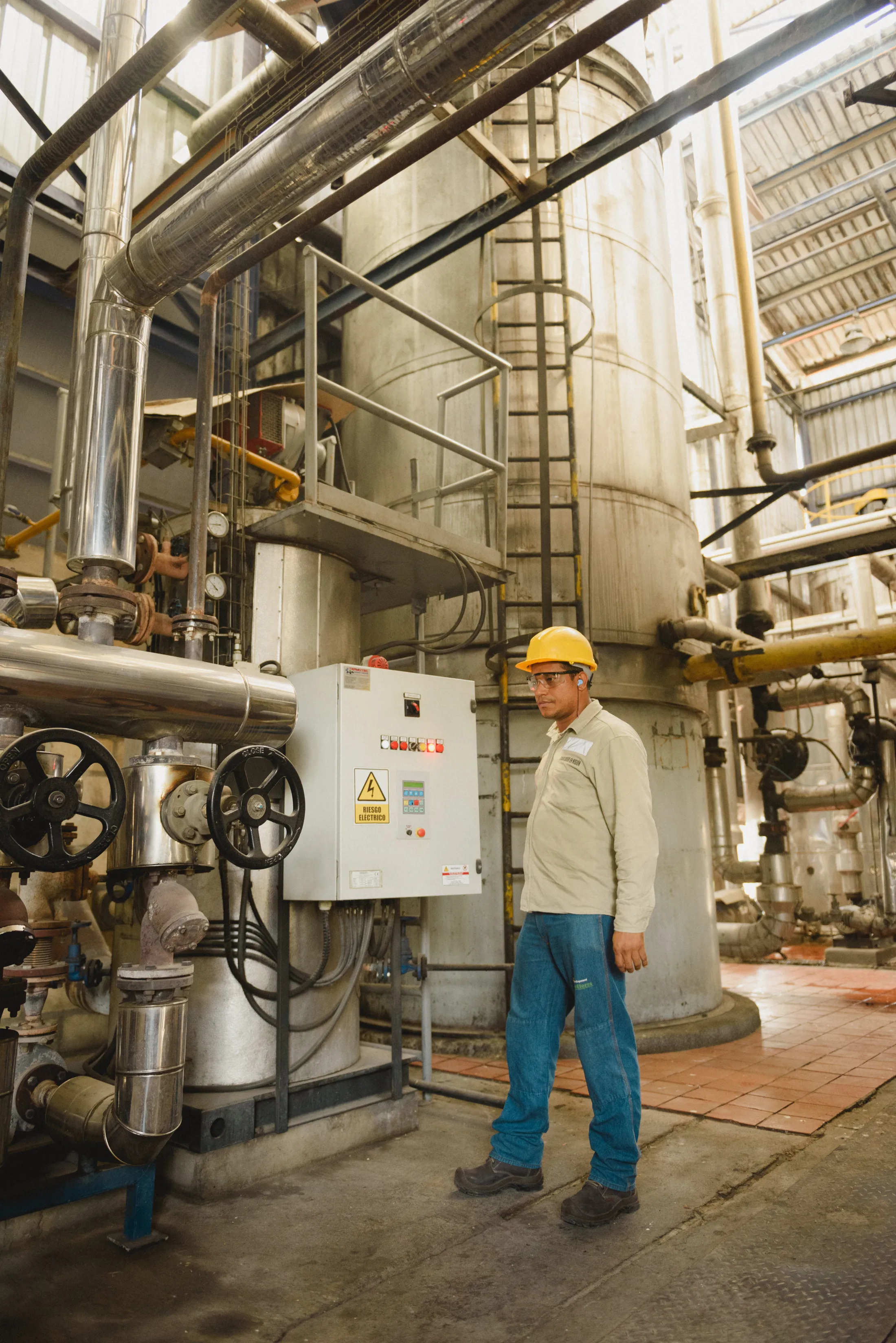 A technician beside the equipment and piping of a process plant.